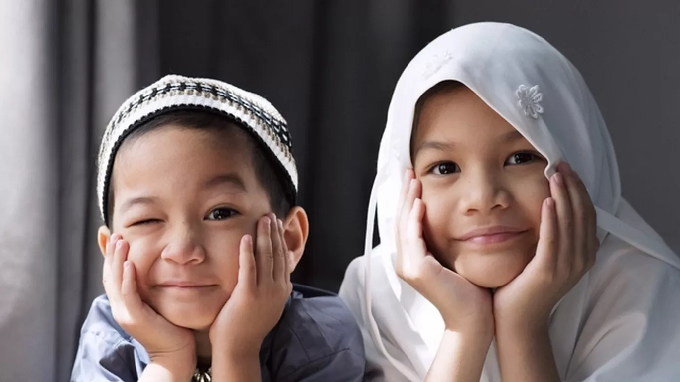 Seorang anak laki-laki dan perempuan muslim berpose menyangga dagu dan menghadap ke kamera