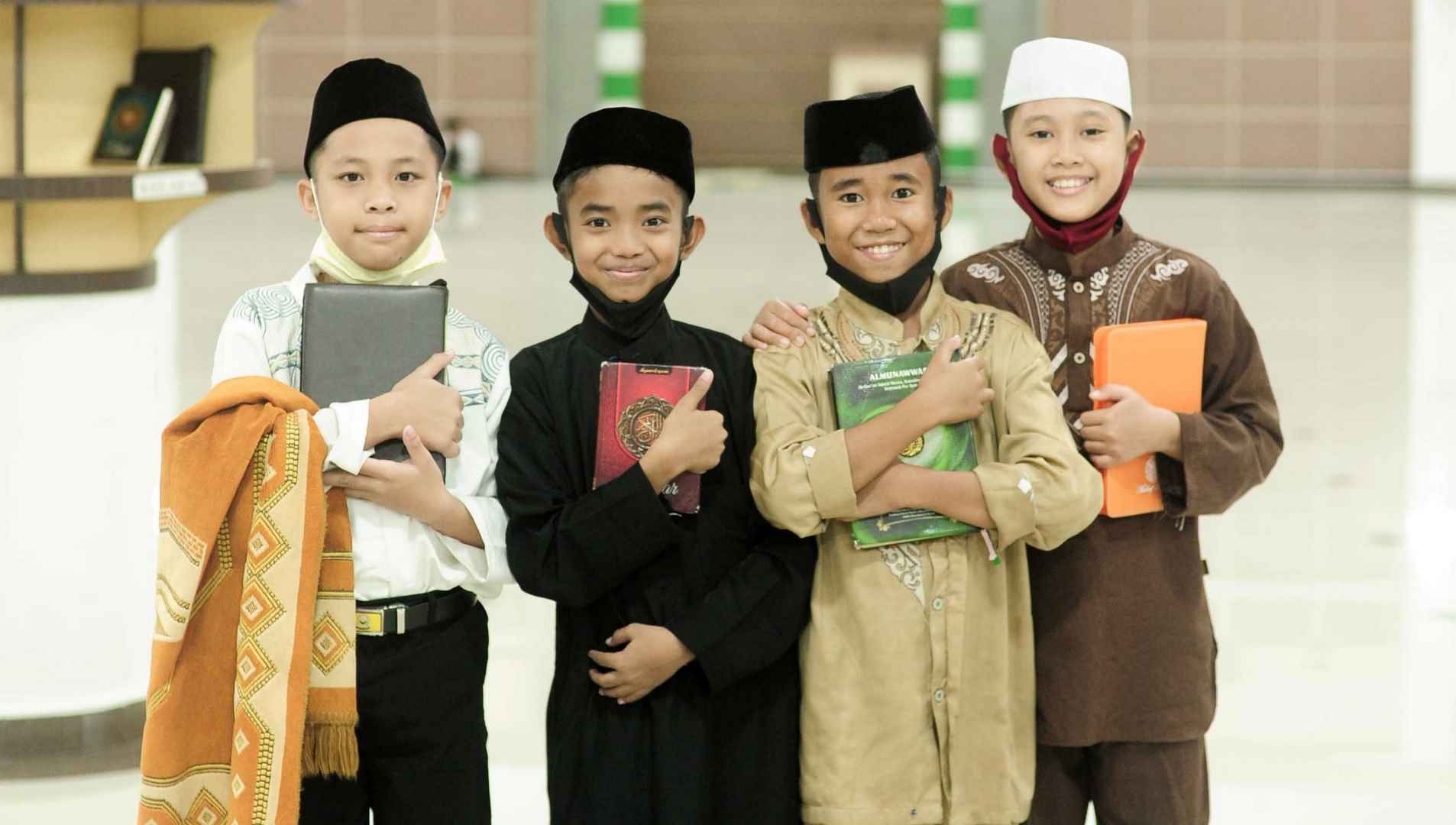 4 anak laki-laki sedang memeluk Al-quran dan tersenyum menghadap kamera