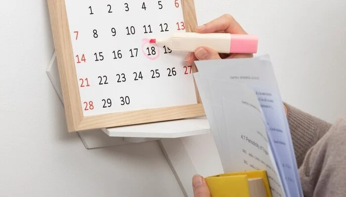 Gambar tangan sedang melingkari tanggal 18 di kalender menggunakan stabilo berwarna pink